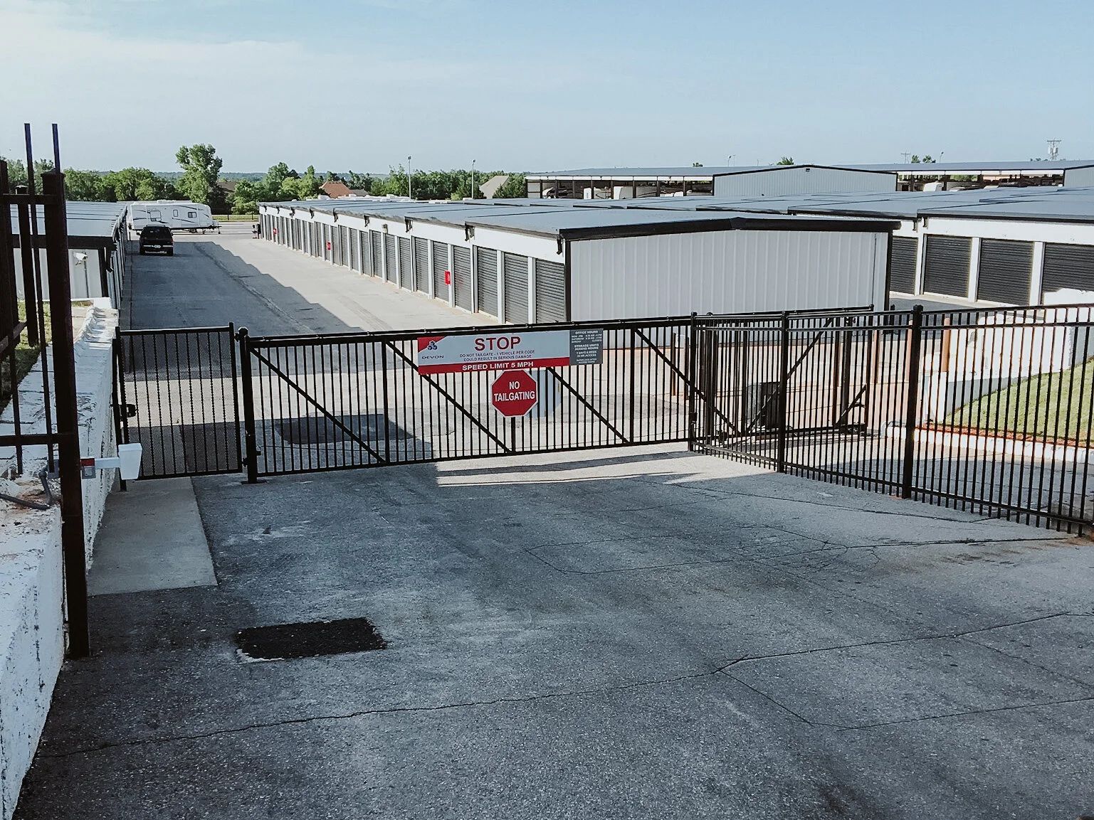 Closed gated driveway leading to a waterfront dock area with white storage units and a red warning sign