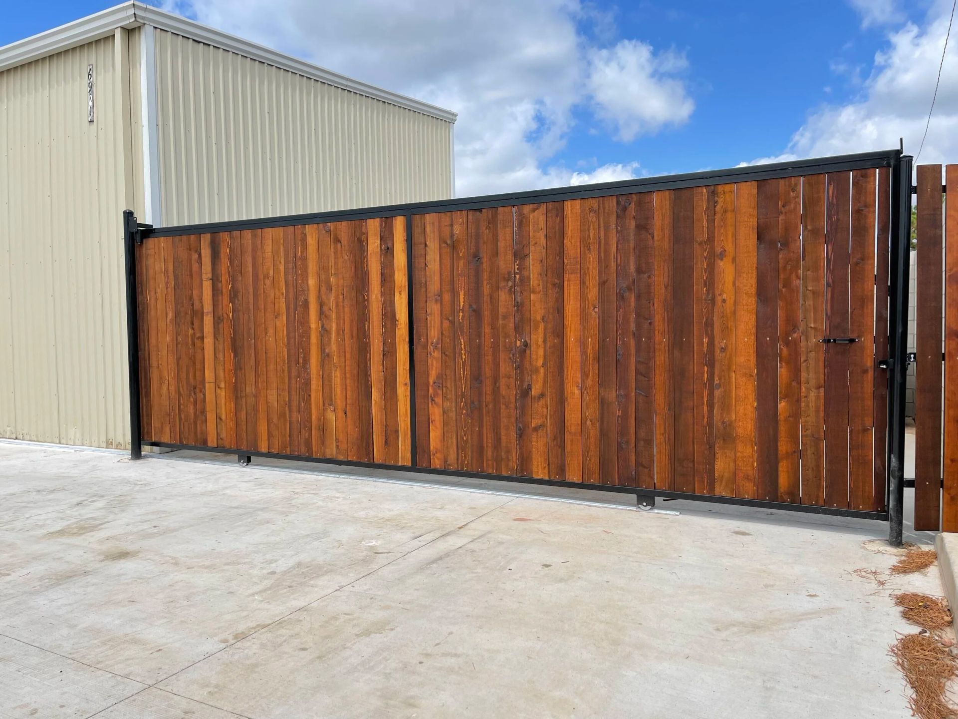 Wooden sliding gate with black frame beside a beige metal building on a concrete lot