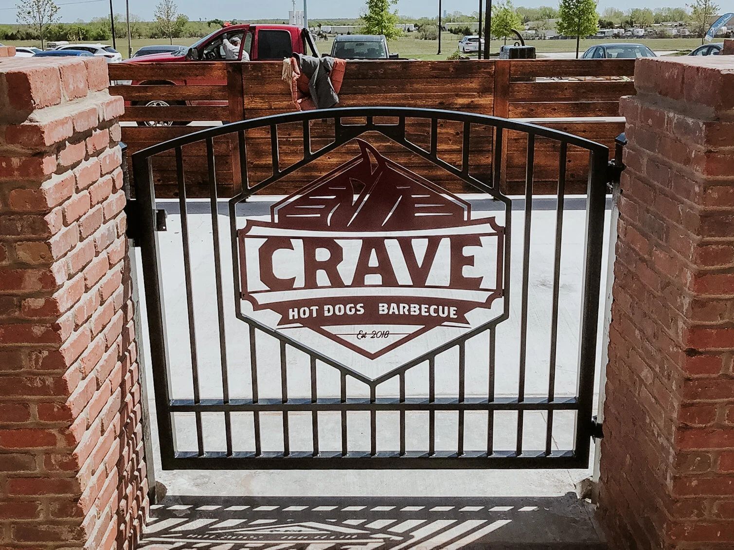 Metal gate with a Crave hot dogs and barbecue sign in front of a brick entrance