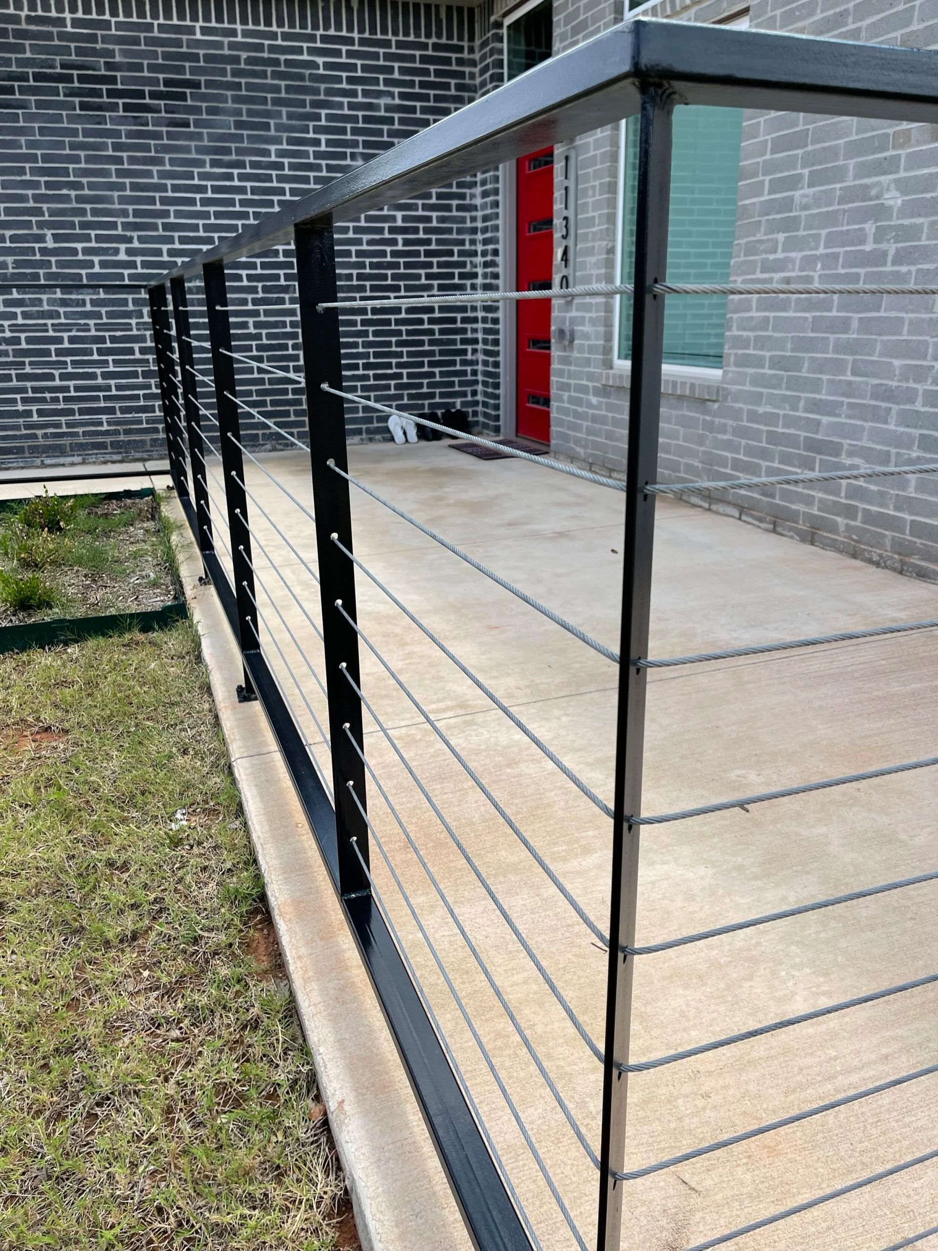 Black metal railing beside a concrete walkway leading to a red door on a gray brick building
