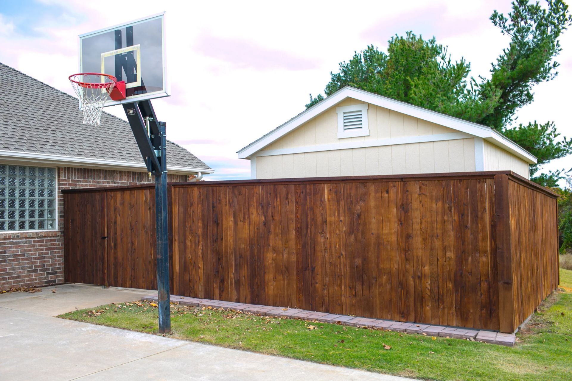 Backyard basketball hoop beside a wooden privacy fence next to a house