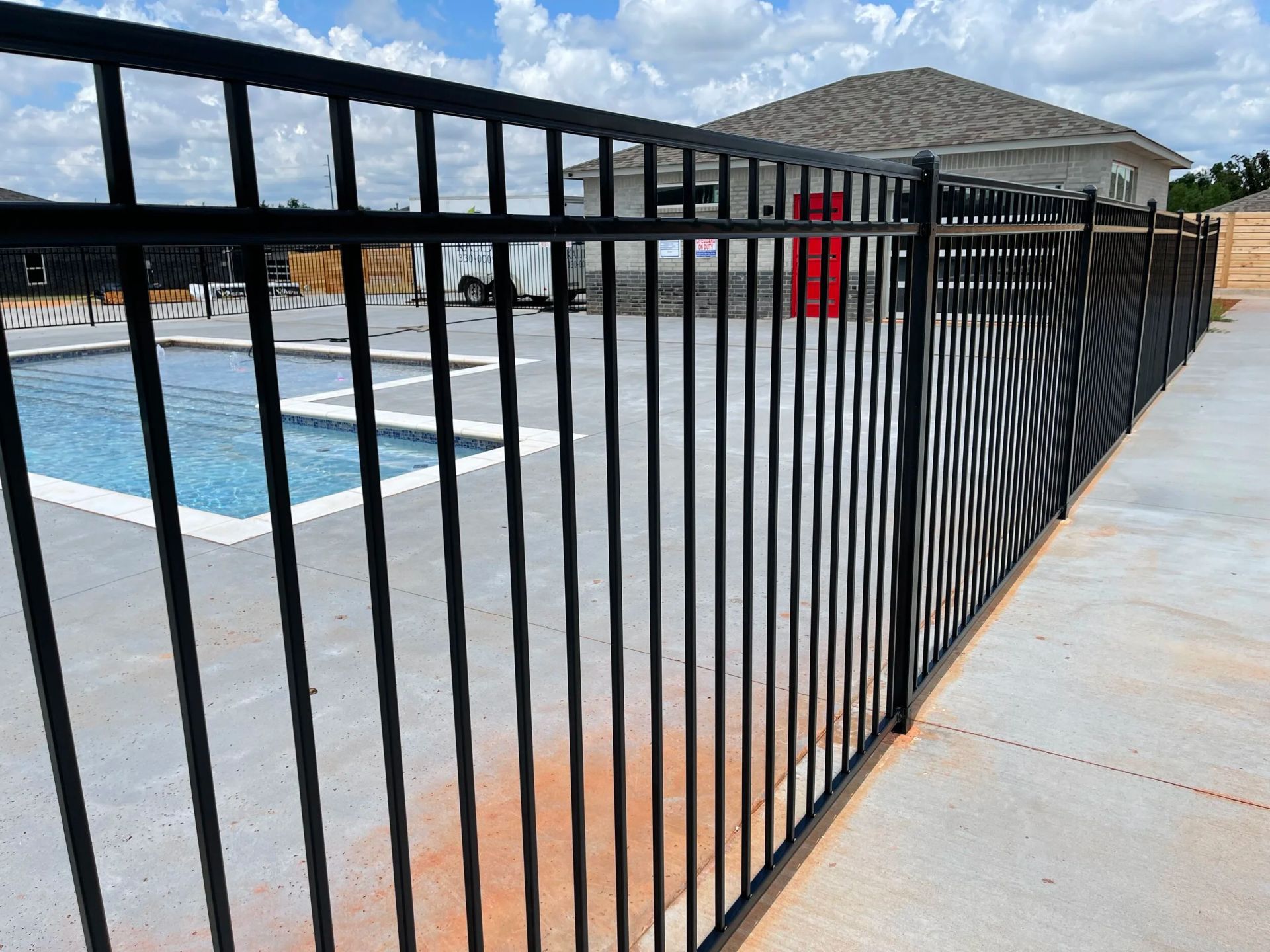 Black metal fence beside a backyard pool and patio, with houses in the background