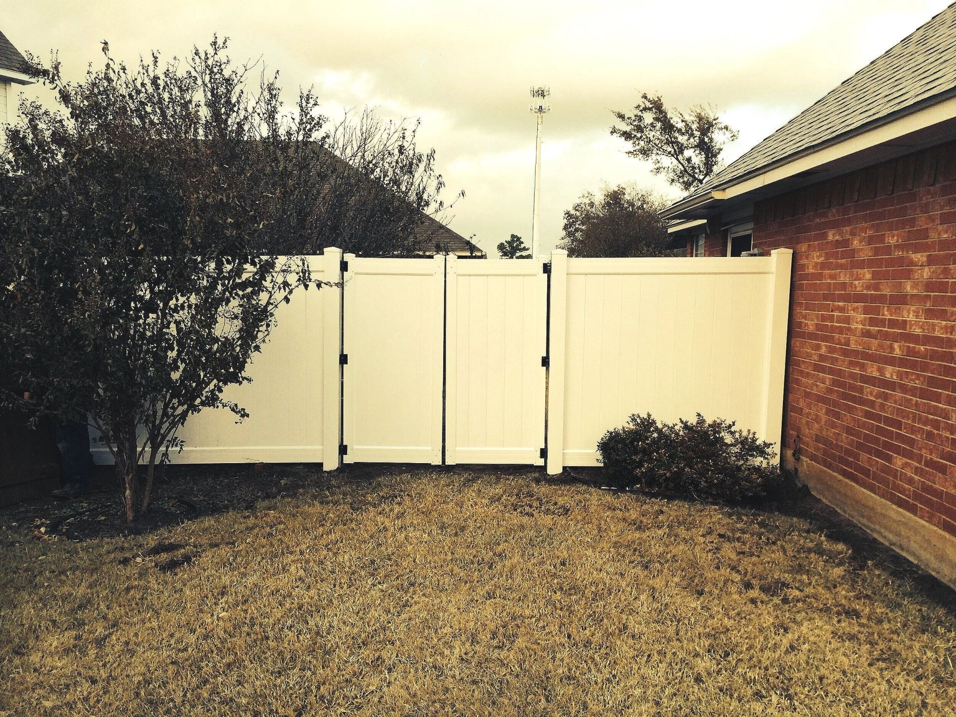 Small gravel yard with a white fence, shrubs, and a brick house wall on the right.