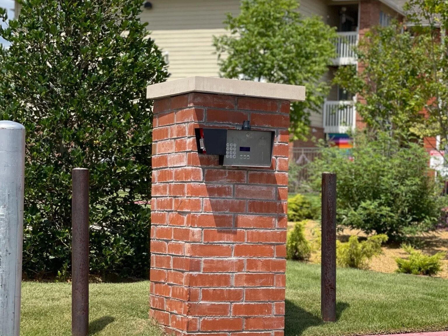 Brick mailbox pillar with black mailbox in a suburban yard, bordered by grass and shrubs.