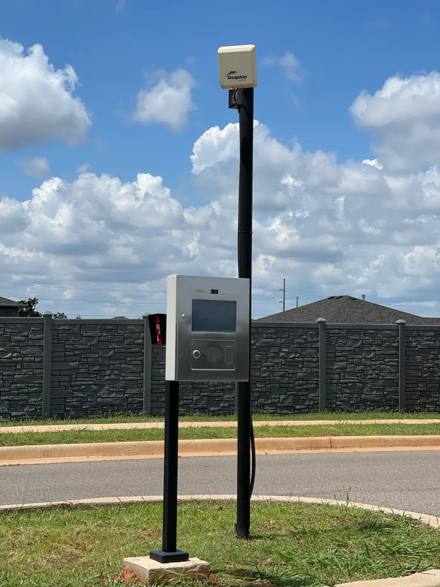 Parking payment kiosk with solar panel and camera beside a road under a cloudy sky