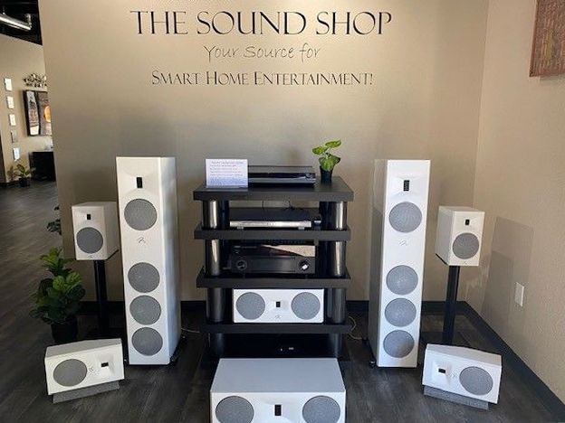 A display of white speakers and audio equipment in a shop, set against a wall with store signage.