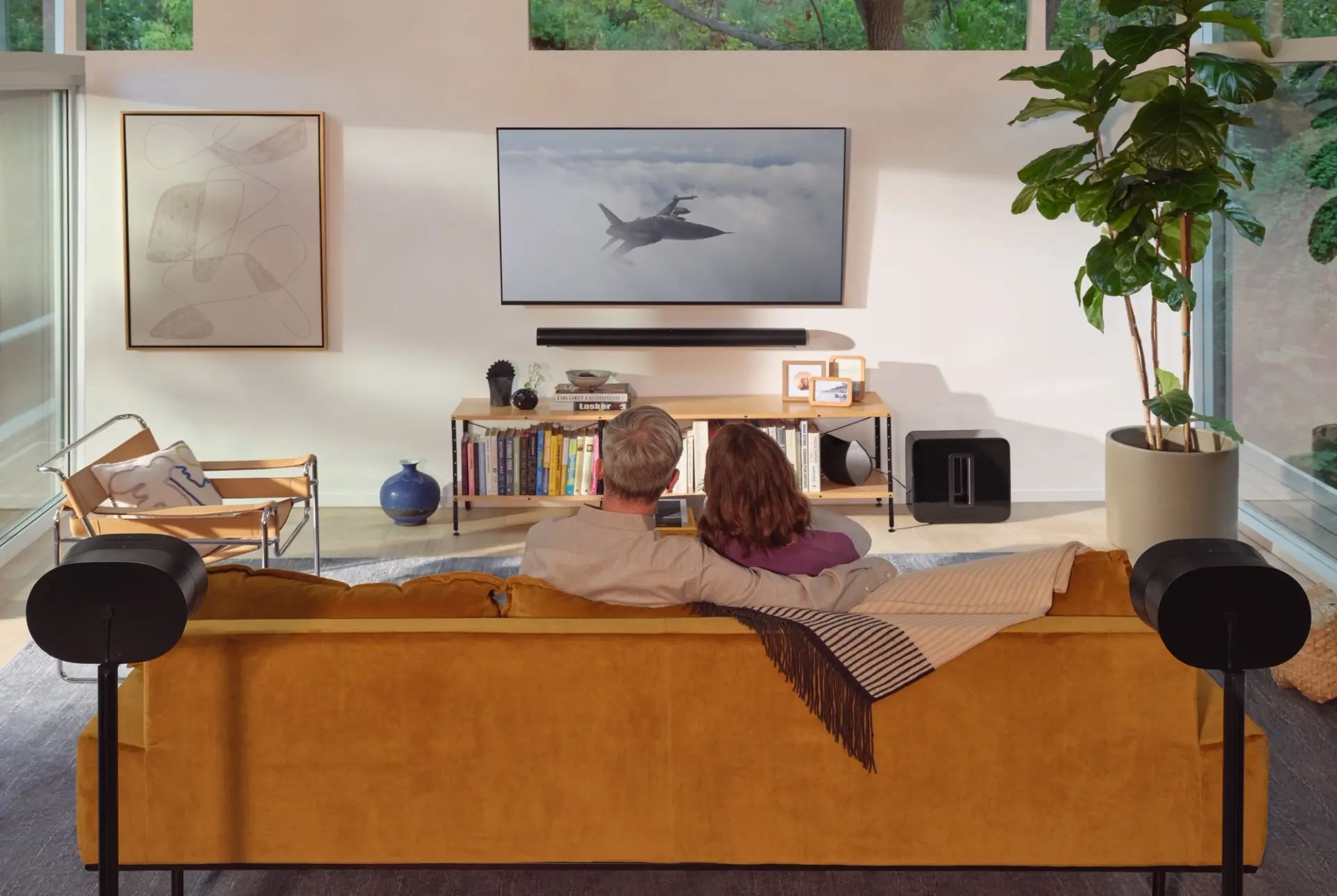 A man is laying on a couch in a living room watching a television.