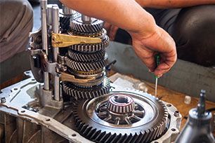 A man is working on a gearbox with a screwdriver.