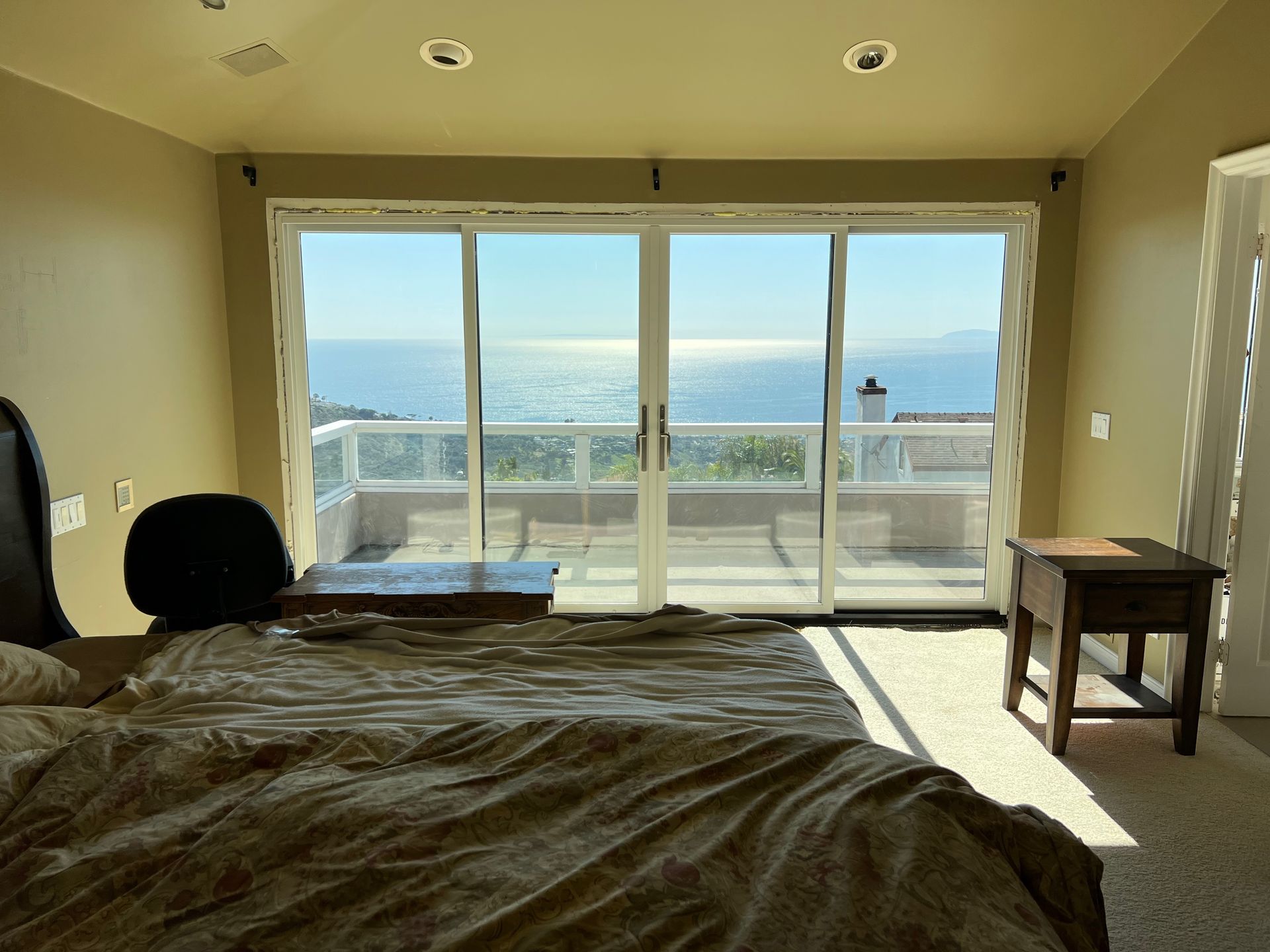A bedroom with a bed and sliding glass doors leading to a balcony overlooking the ocean.