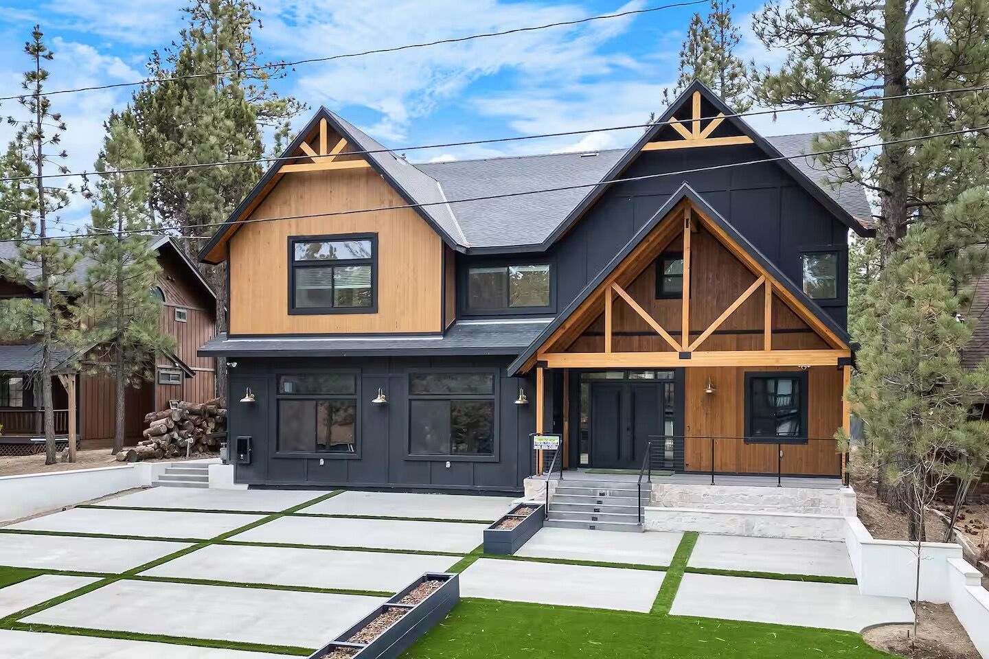 A large house with a black roof and wooden beams is surrounded by trees.