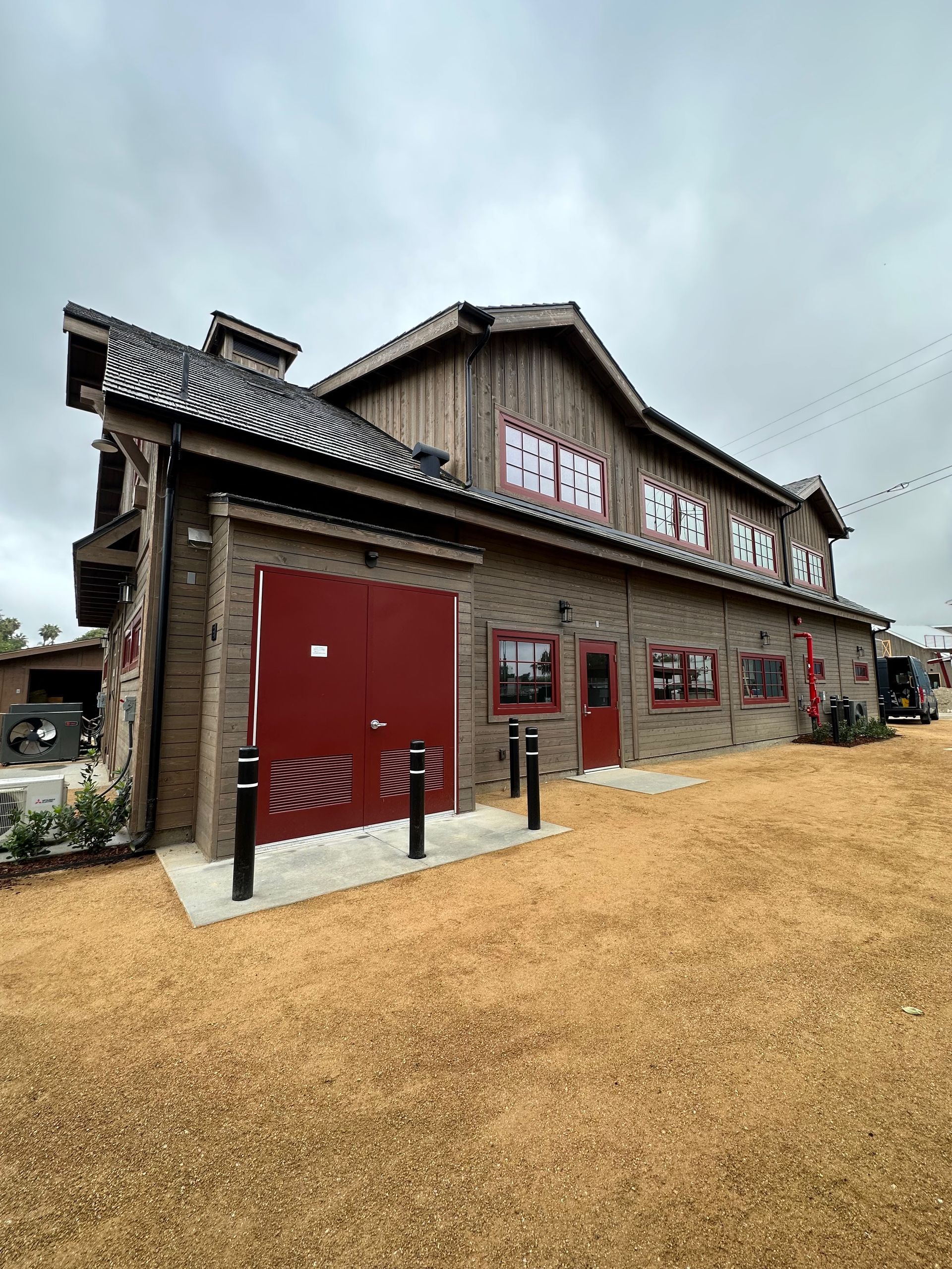 A large building with red doors and windows is sitting on top of a dirt field.