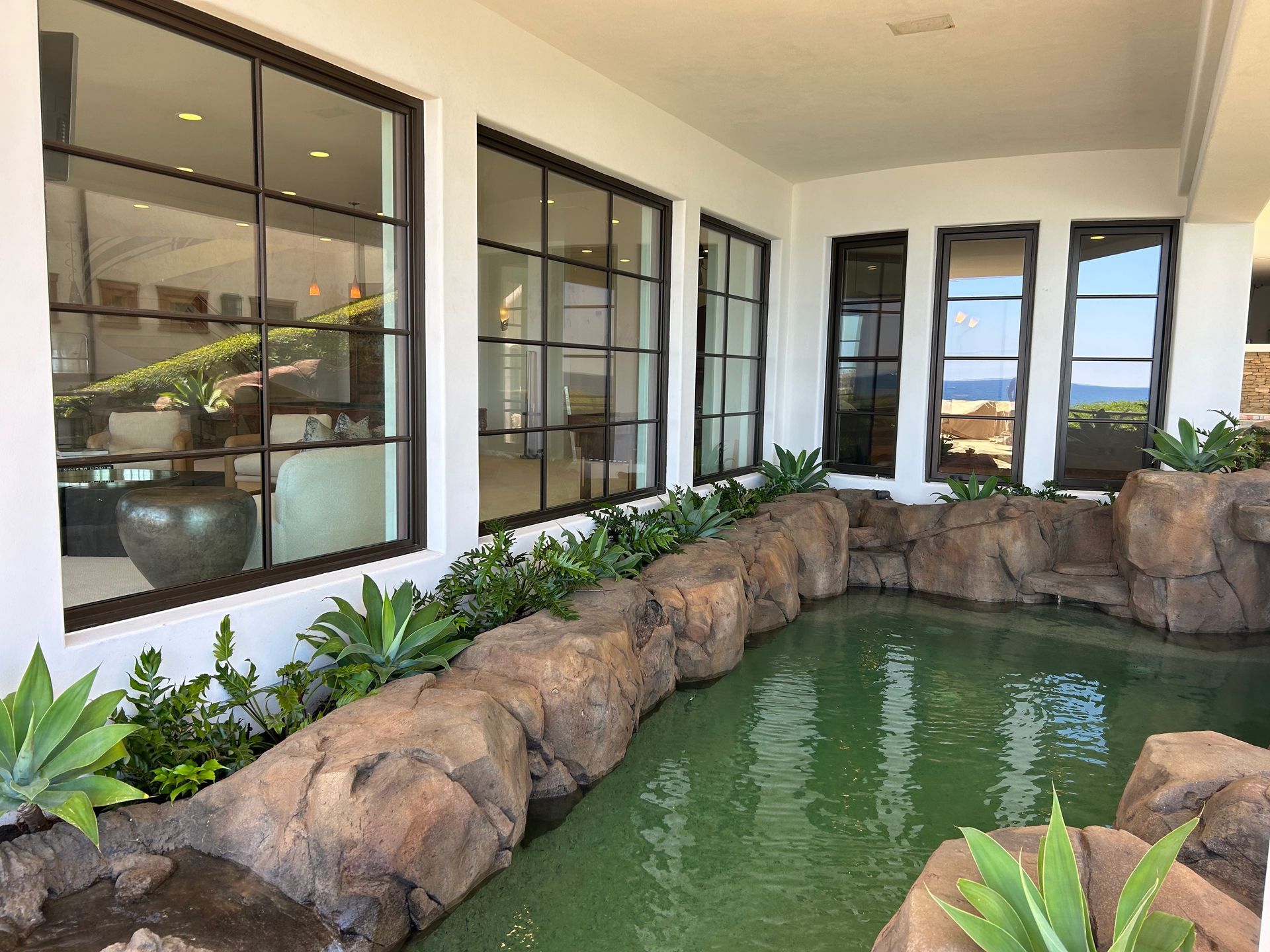 A pond surrounded by rocks and plants in front of a building with lots of windows.