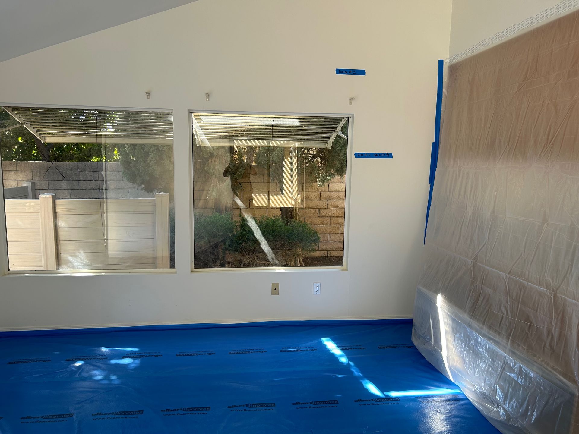 An empty room with a blue tarp on the floor and a window.