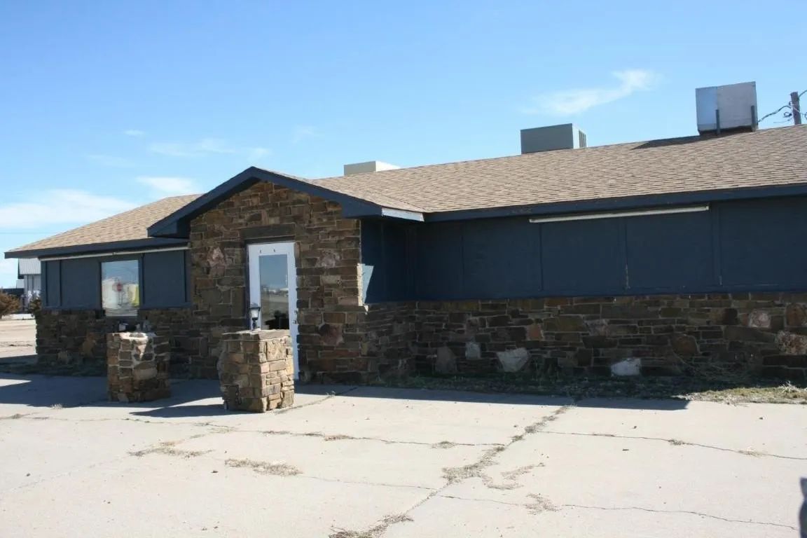 A cream-colored, single-story house with a covered patio, arched openings, and a garage door visible at the end.