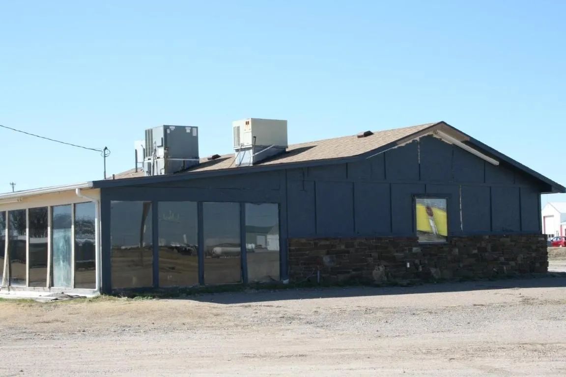 A single-story, gray building with a dark stone base, large glass-paneled windows, and roof-mounted HVAC units.