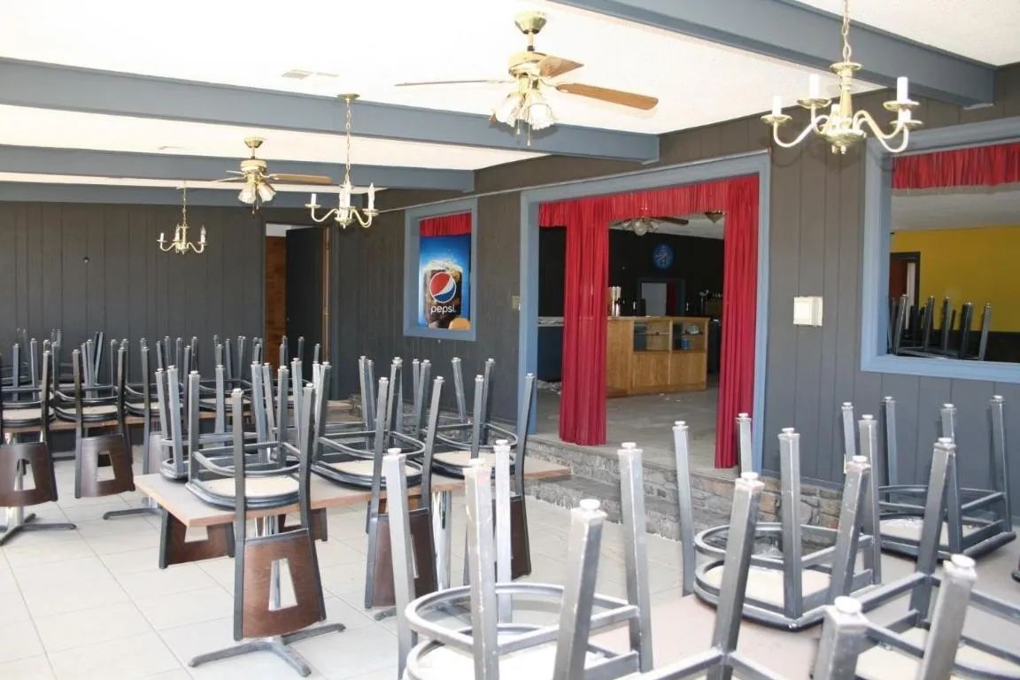 Dining area with chairs placed upside down on tables, dark walls, red curtains, and chandeliers.