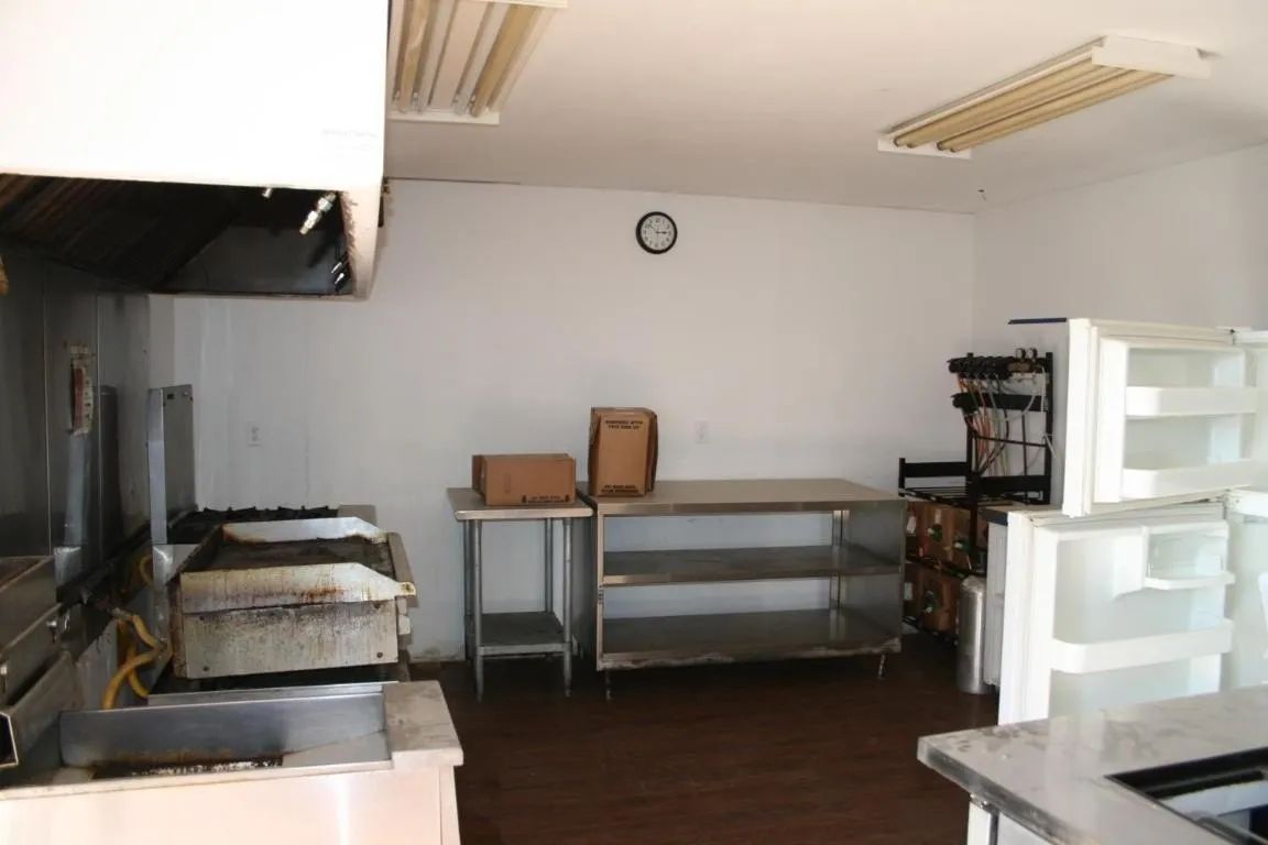 A commercial kitchen with stainless steel tables, a flat-top grill, boxes on counters, and open refrigeration units.
