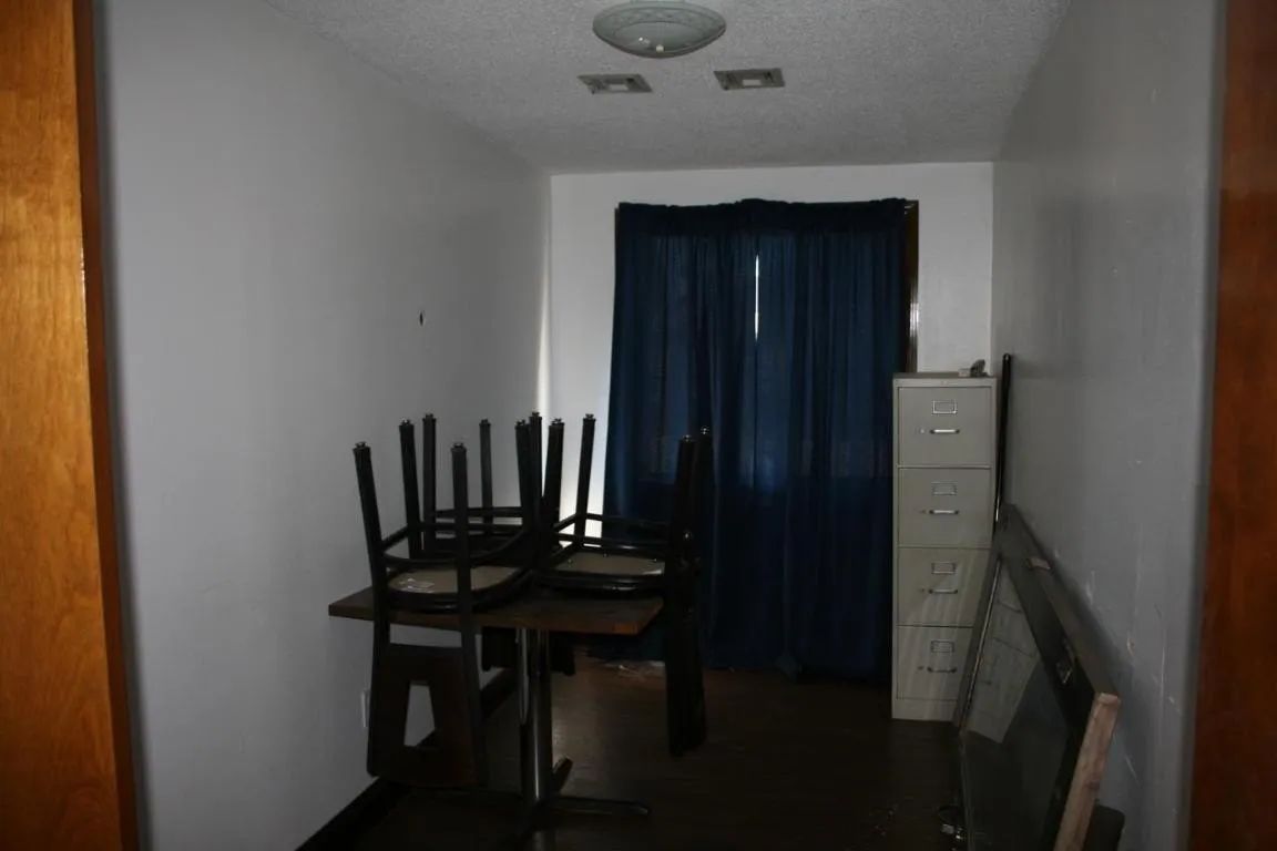 A dining table with chairs turned upside down on top of it, positioned in a room with blue curtains and a filing cabinet.
