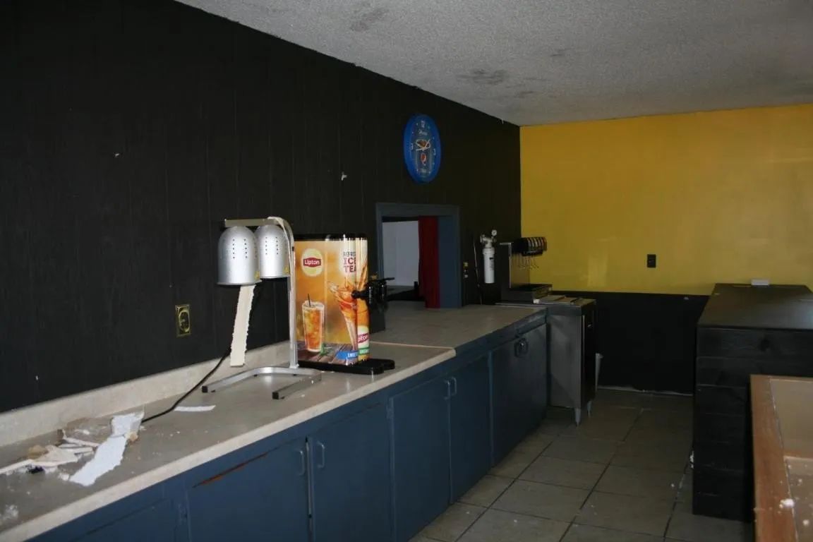 An empty counter space features black and yellow walls, a metal dispenser, and blue cabinets in a dimly lit room.