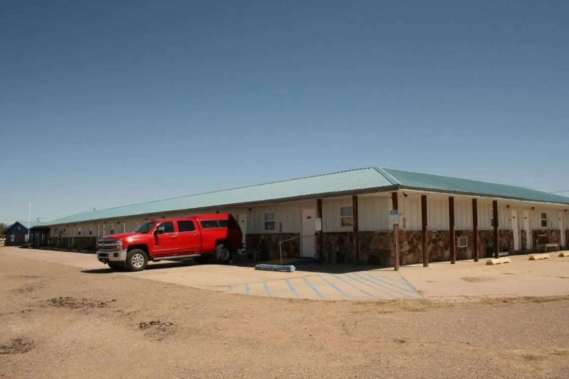 A long, low-slung, single-story motel building with a blue metal roof and a red pickup truck parked in front.