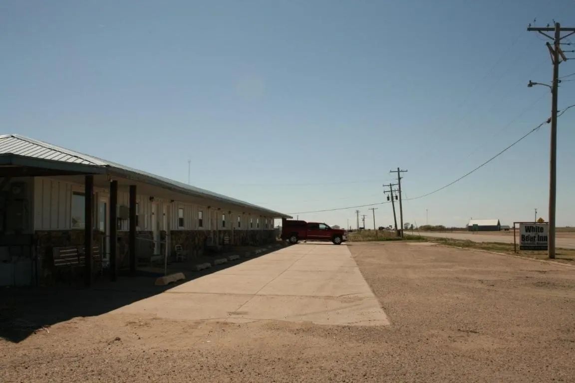 A single-story motel building with a concrete parking area, a red truck, and utility poles under a clear blue sky.