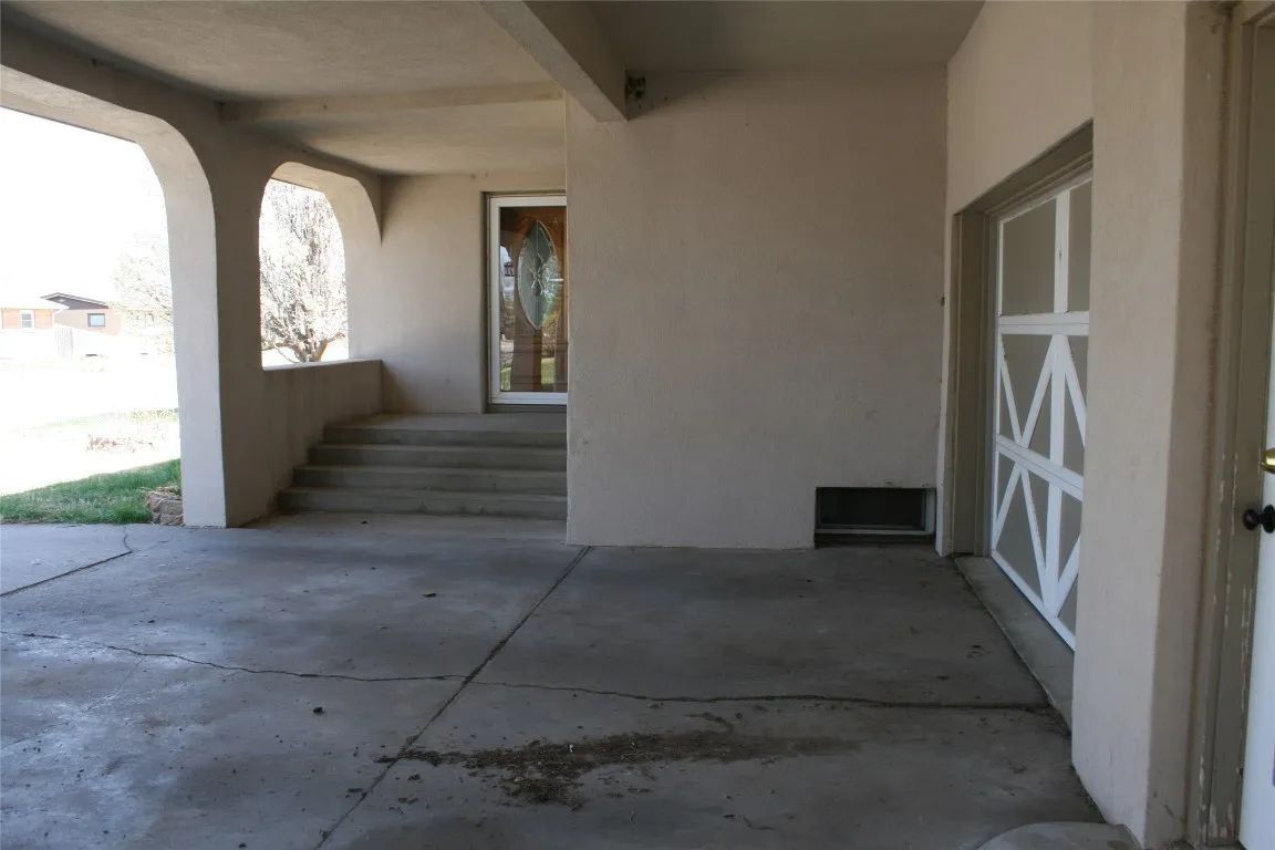 Concrete carport with a stucco wall, stairs leading to a front door, and a garage door with a white grid pattern.