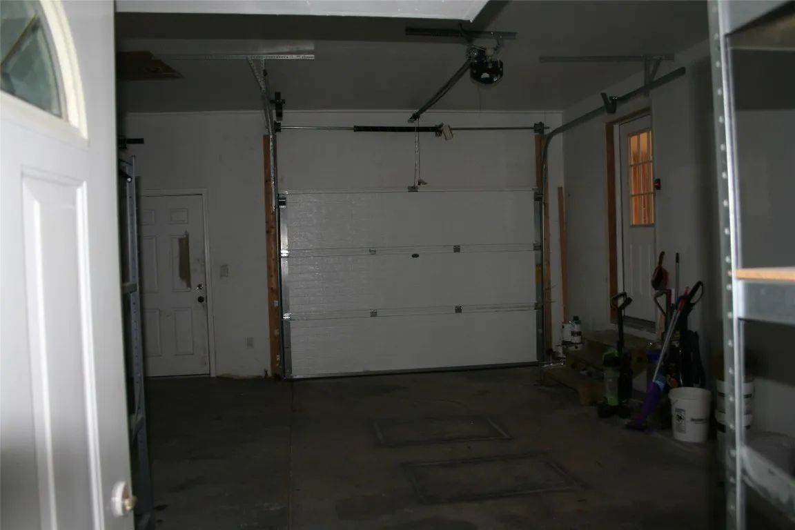 A dimly lit garage interior with a closed white sectional door, a side entry door, and scattered cleaning tools.