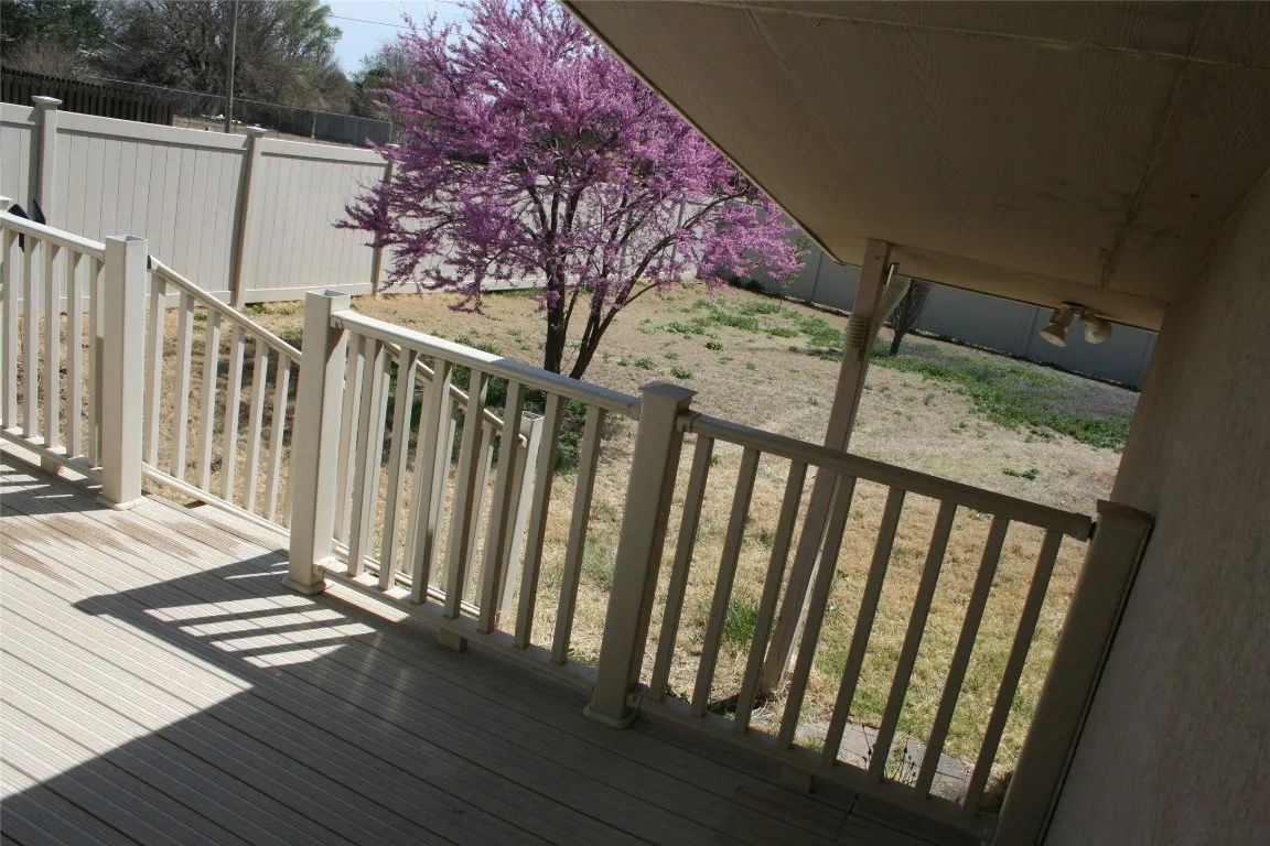 A wooden deck with a beige railing overlooks a backyard featuring a flowering redbud tree against a tan privacy fence.