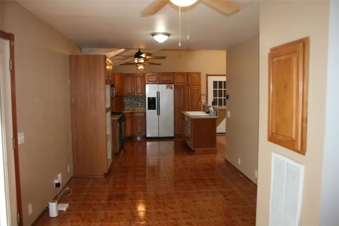A kitchen with brown tile flooring, wood cabinets, a stainless steel refrigerator, and a small center island.