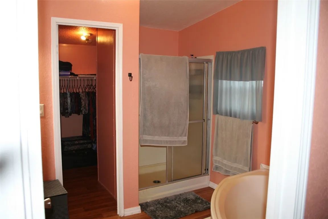 A bathroom with coral walls, a glass walk-in shower with a grey towel, a walk-in closet, and a partial bathtub.