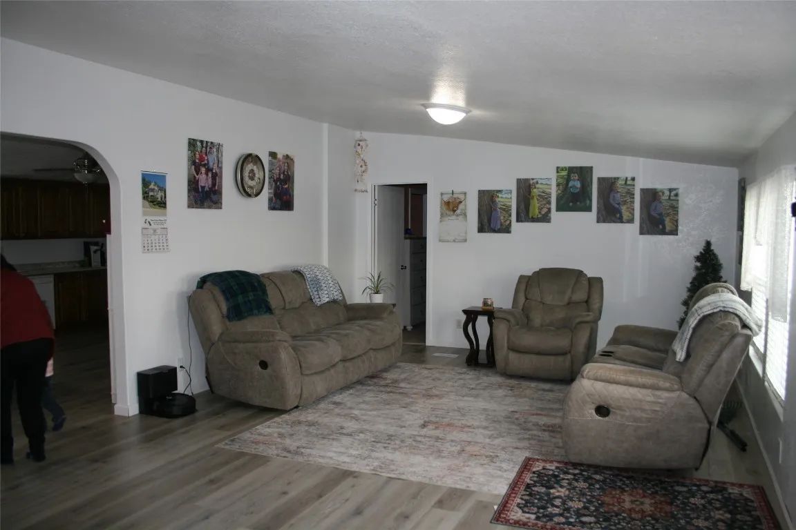 A living room with a beige couch and two armchairs on a patterned rug, with multiple pictures hanging on white walls.