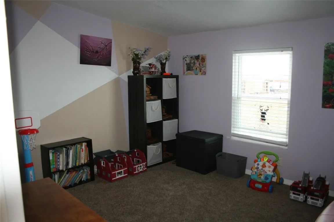 A child’s bedroom with a geometric accent wall, shelving, toy storage, books, a window, and a baby walker on carpet.