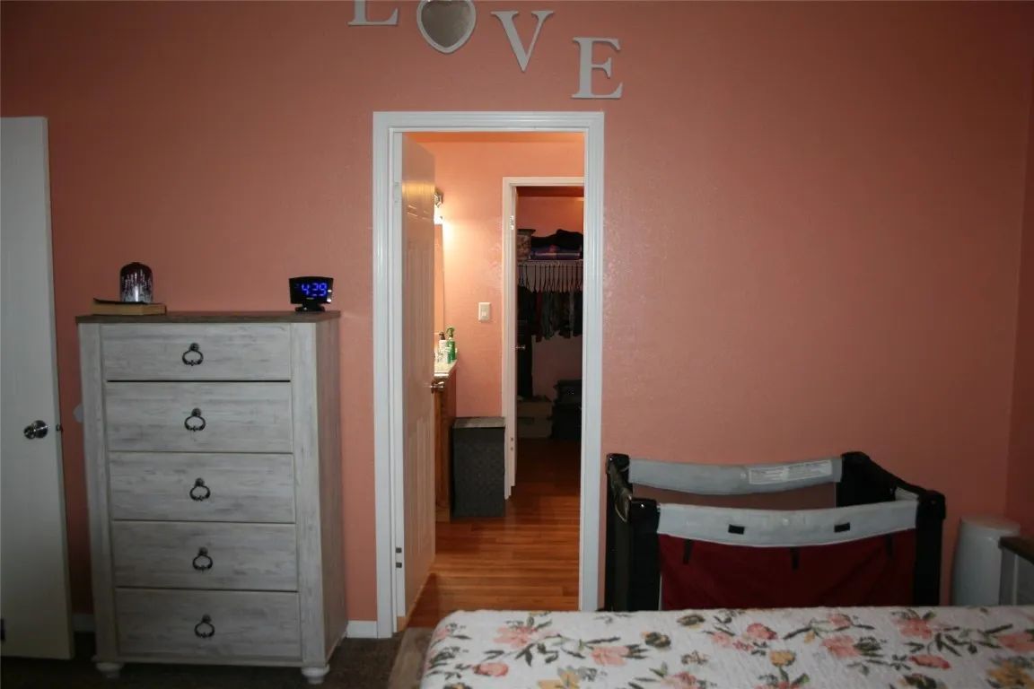 A peach-colored bedroom featuring a tall dresser, a portable crib, and the word 