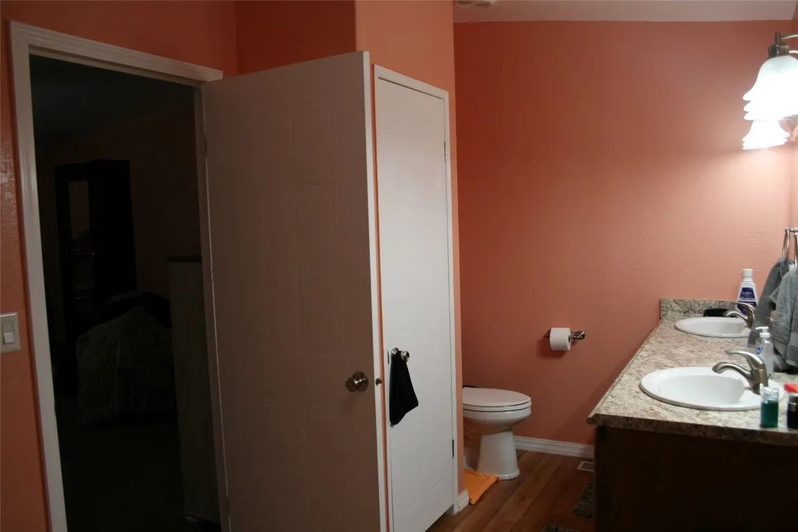 A bathroom with coral walls, a white vanity with two sinks, a toilet, and a white closet door beside a room doorway.
