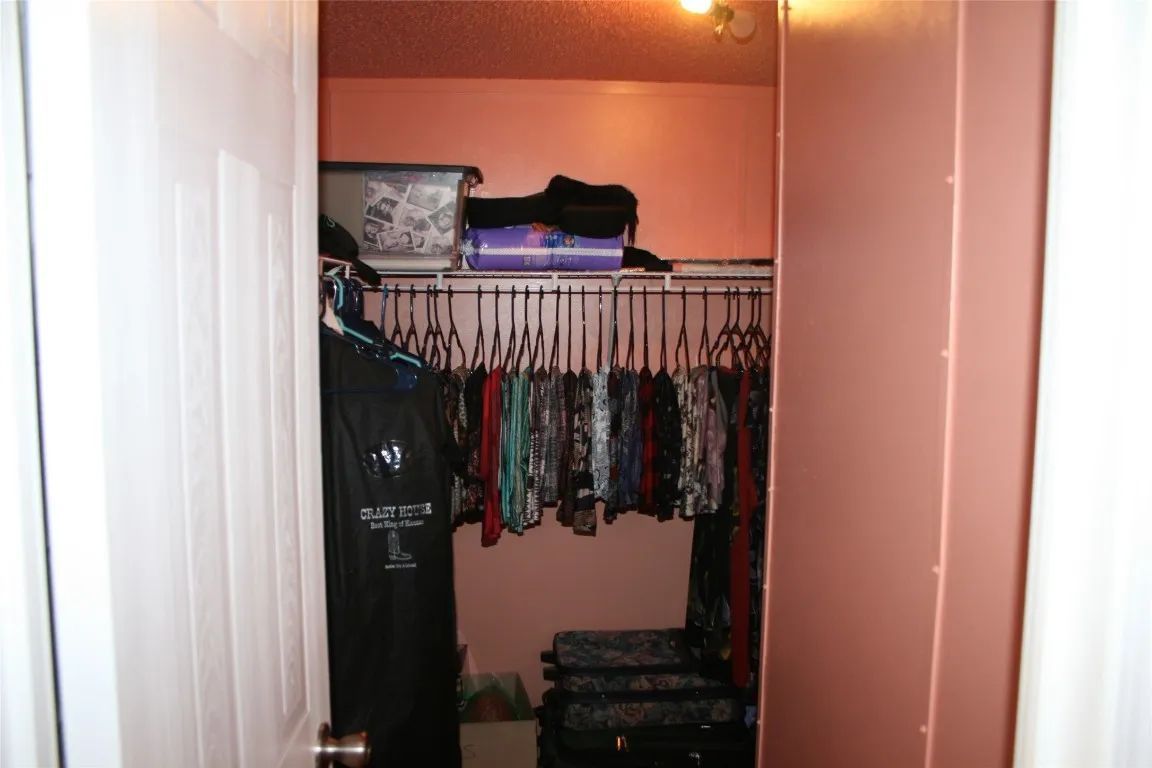 A closet with salmon-colored walls, filled with hanging clothes, a shelf with boxes, and suitcases on the floor.