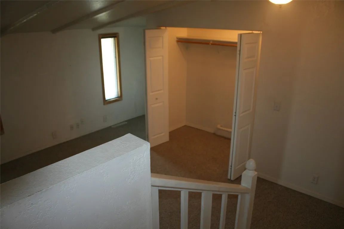 A view from a staircase looking into an upper-level room with beige carpet, white walls, a closet, and a narrow window.