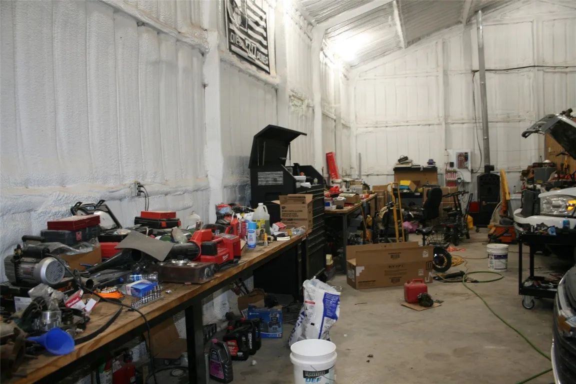 A cluttered automotive repair shop with a long workbench, scattered tools, equipment, and a car being serviced.