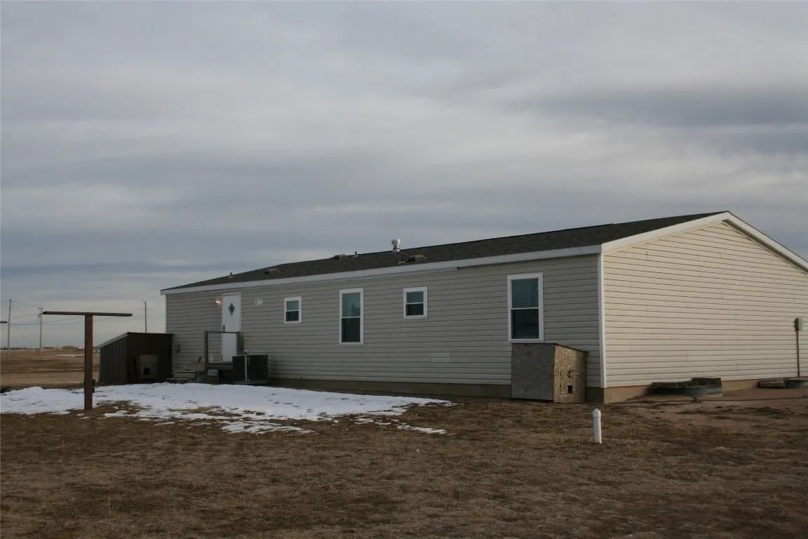 A single-story, light gray manufactured home with horizontal siding sits on a barren, snow-dusted lot under a cloudy sky.