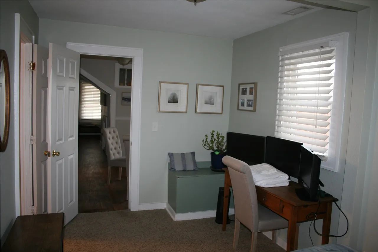 A home office featuring a wooden desk with two monitors, a chair, and a green storage bench against a light grey wall.