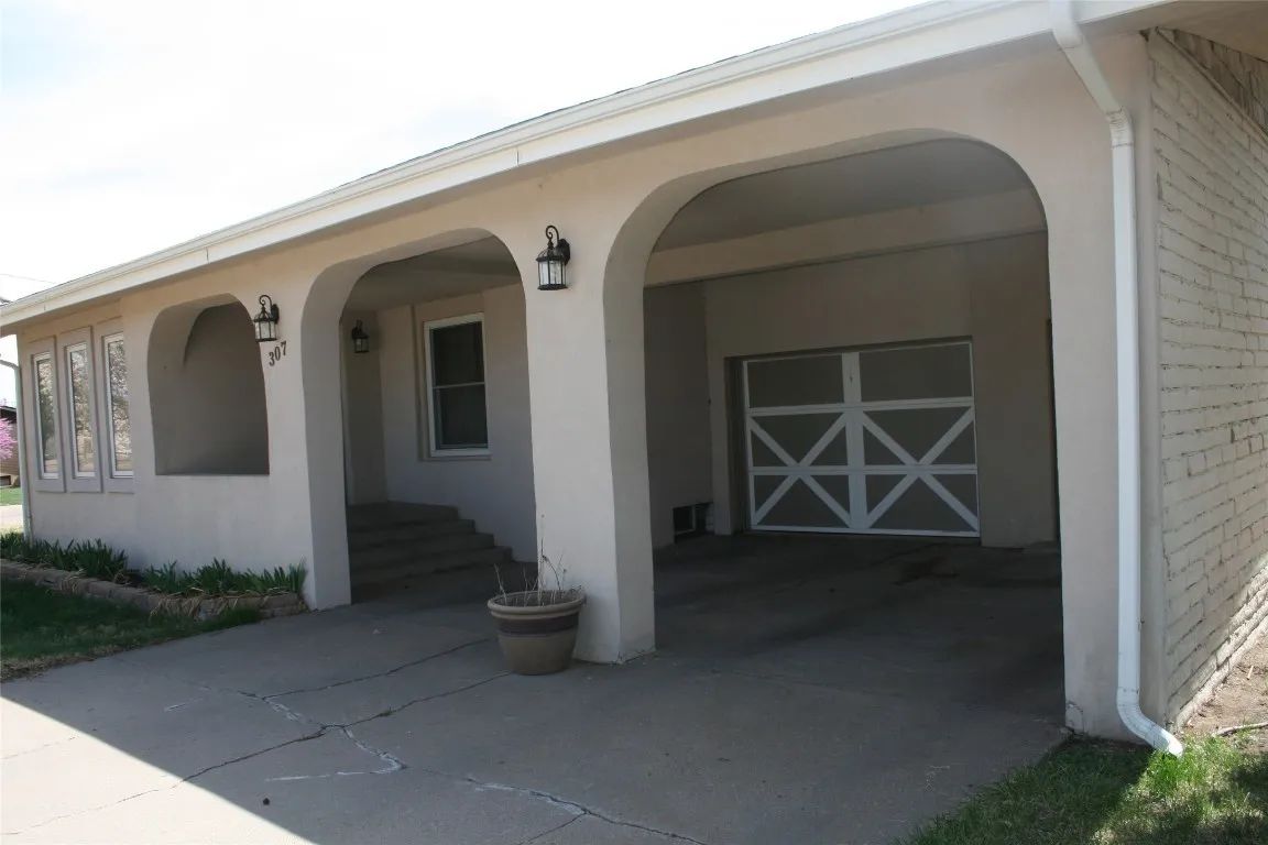 A cream-colored, single-story house with a covered patio, arched openings, and a garage door visible at the end.
