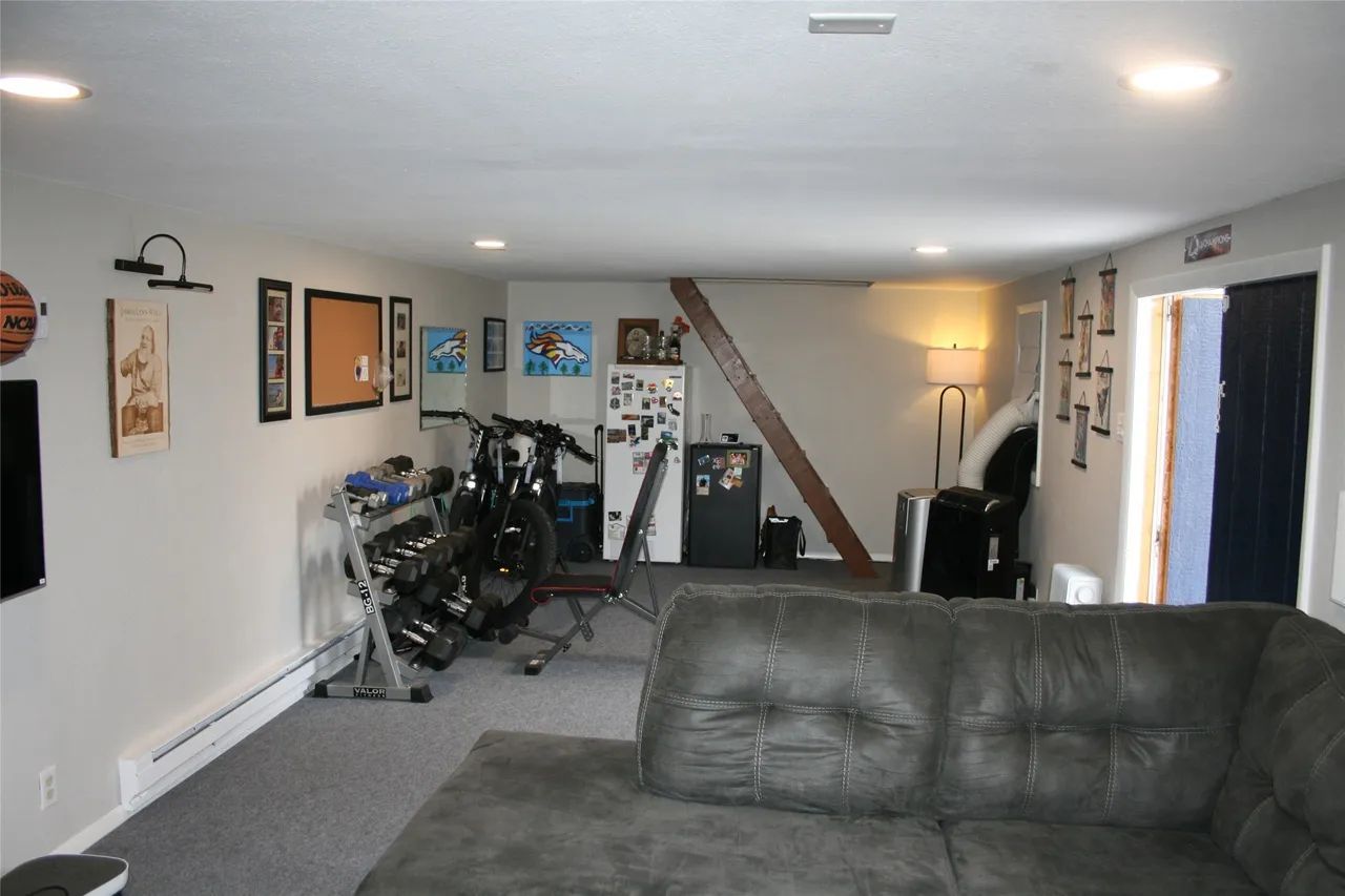 Basement living area featuring a large grey sectional sofa, fitness equipment, a refrigerator, and framed wall decor.