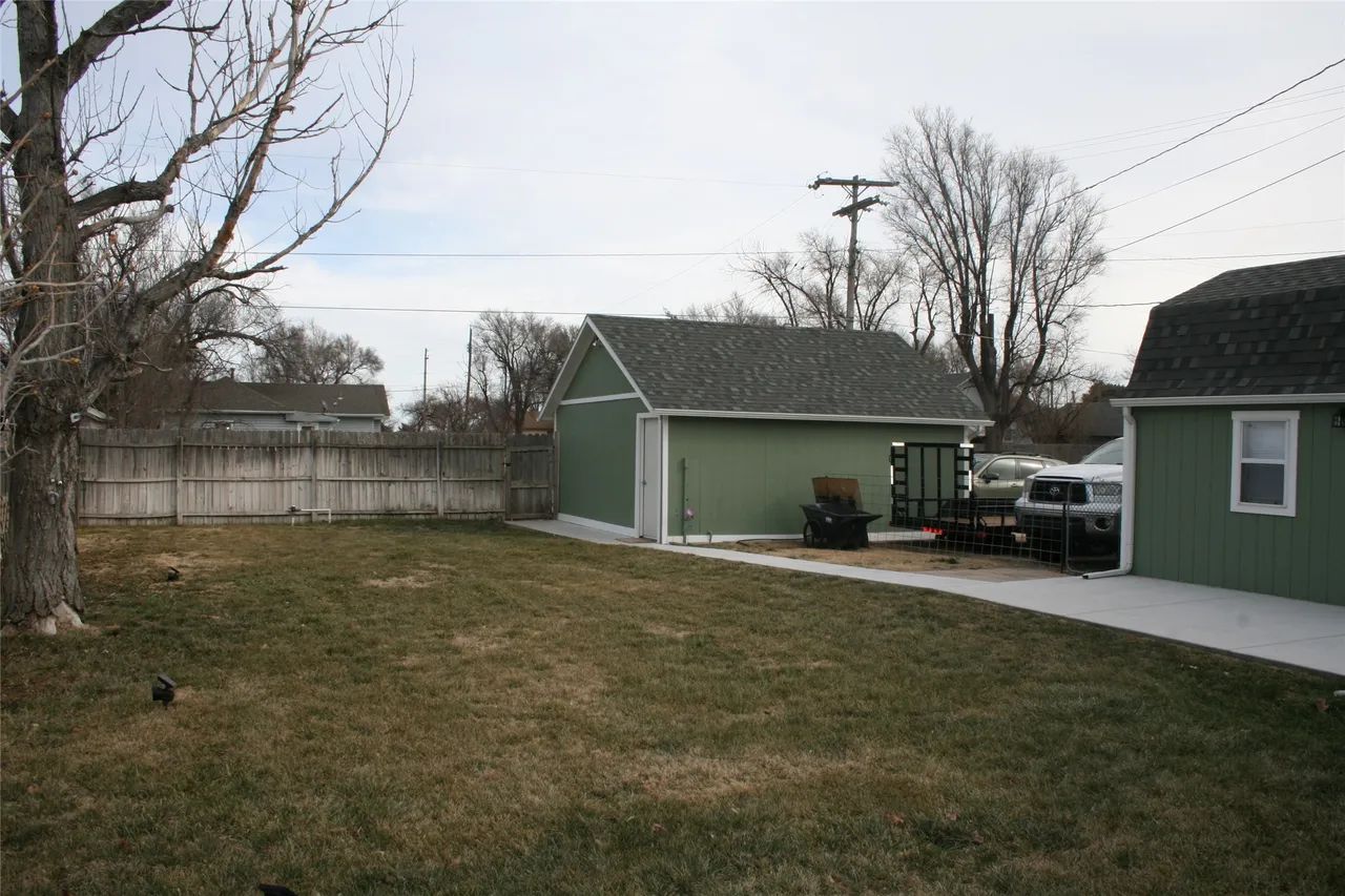 A grassy yard with a green detached garage and a white truck parked on a concrete driveway under an overcast sky.