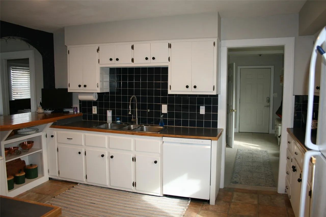 Kitchen with white cabinets, dark tile backsplash, wooden countertops, and a doorway leading to a hallway.