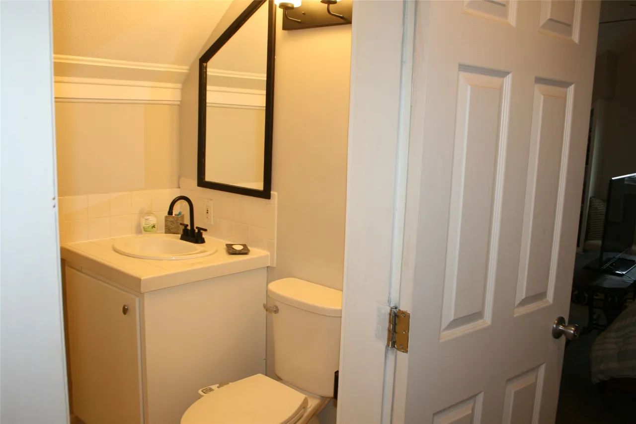 A small bathroom with a white vanity, a sink, a toilet, a mirror on the wall, and a white door slightly ajar.