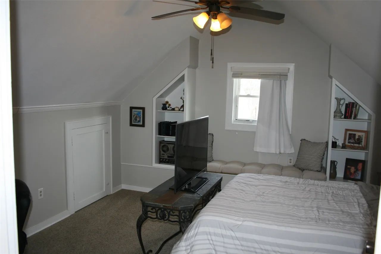 Attic bedroom with gray walls, a bed, a television on a metal table, and built-in white shelves flanking a window.
