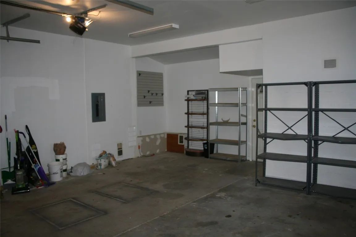 An empty garage with a concrete floor, two metal storage racks, a breaker box on the wall, and cleaning tools in a corner.