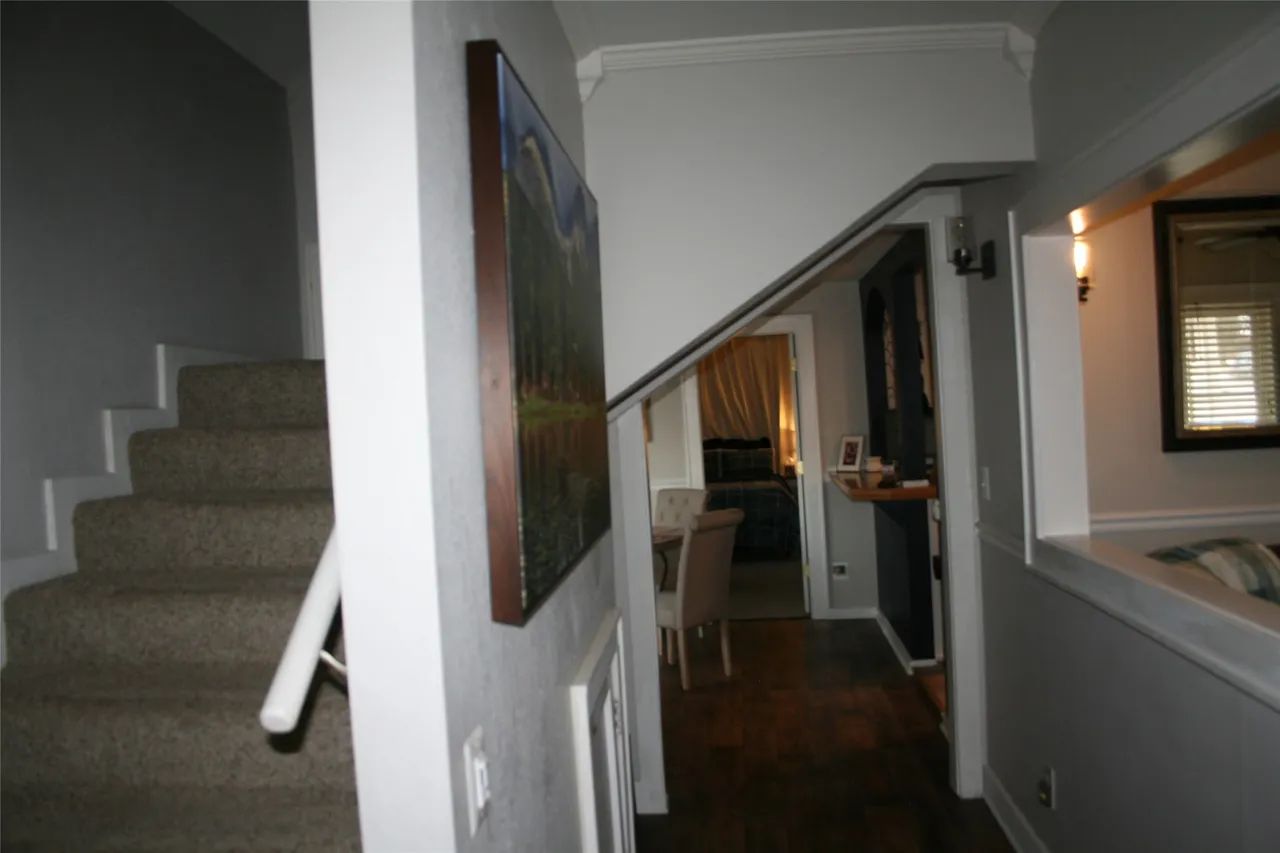 A staircase with carpeted steps next to a hallway leading to a dimly lit room with a wooden table and chairs.