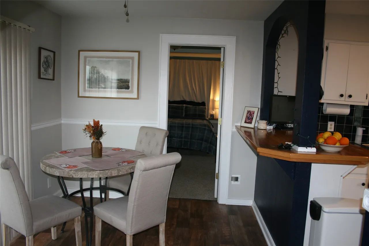 A dining nook with a round metal table and four beige chairs, next to a kitchen counter and a doorway to a bedroom.