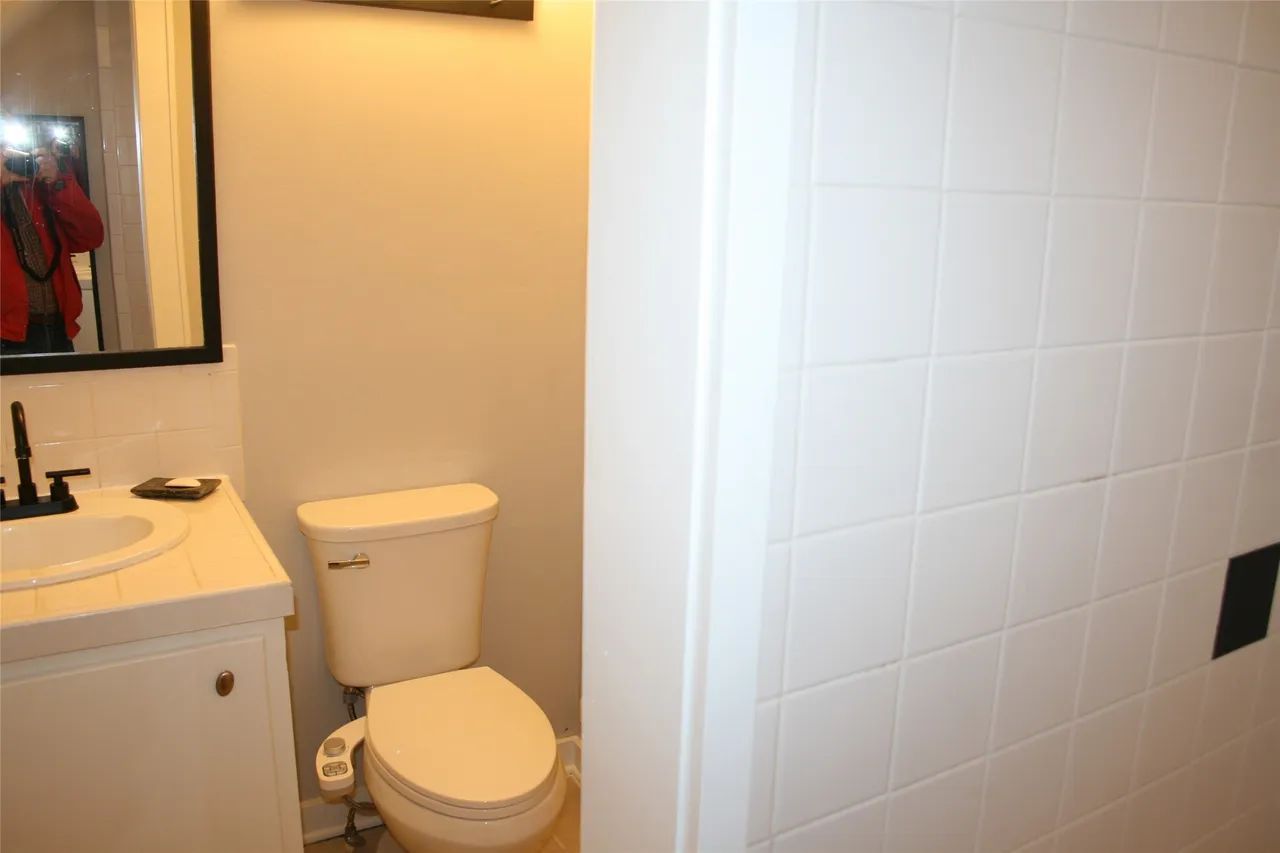 A bathroom featuring a white toilet with a bidet attachment next to a white vanity with a sink and mirror.