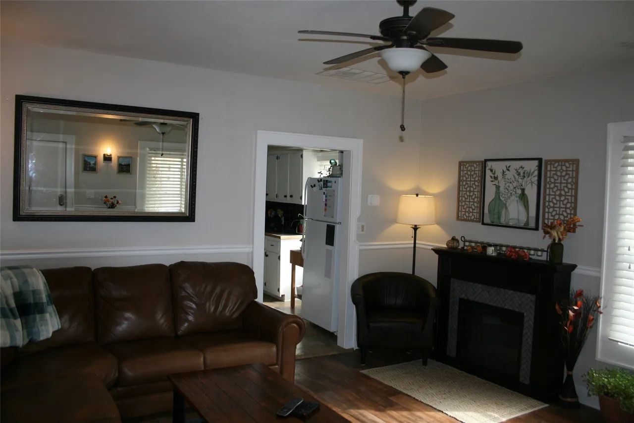 A brown leather sectional sofa, a black fireplace with artwork above it, and a ceiling fan in a gray living room.